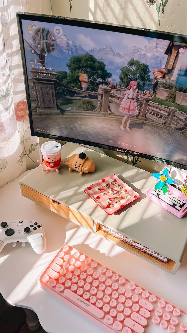 Gaming desk setup with pink keyboard, white controller, and cute desk accessories.