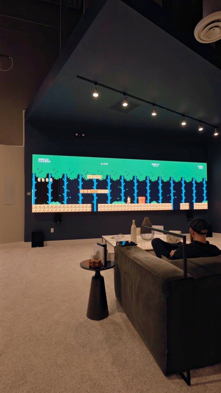 Person sitting on a grey sofa watching a video game on a massive screen