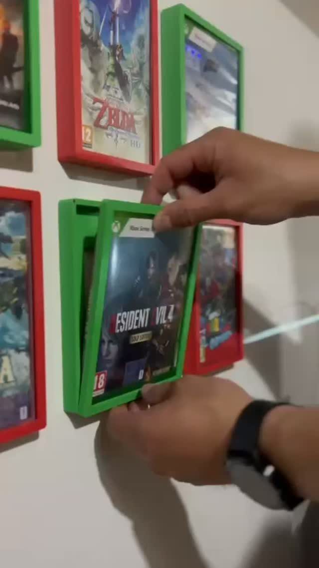 Hands placing a video game case into a green wall-mounted display frame.