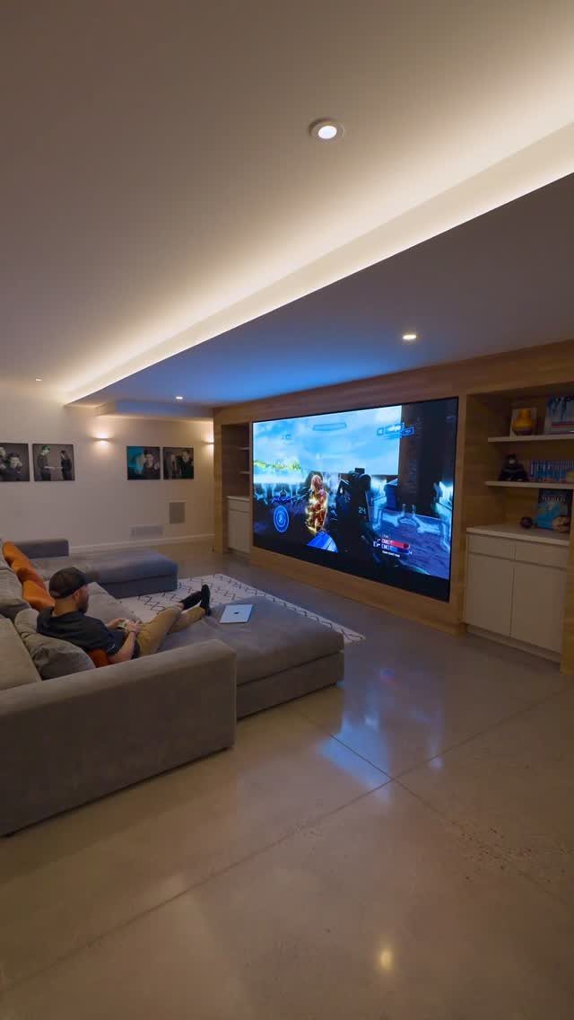 Person relaxing on a grey sofa watching a video game on a huge screen