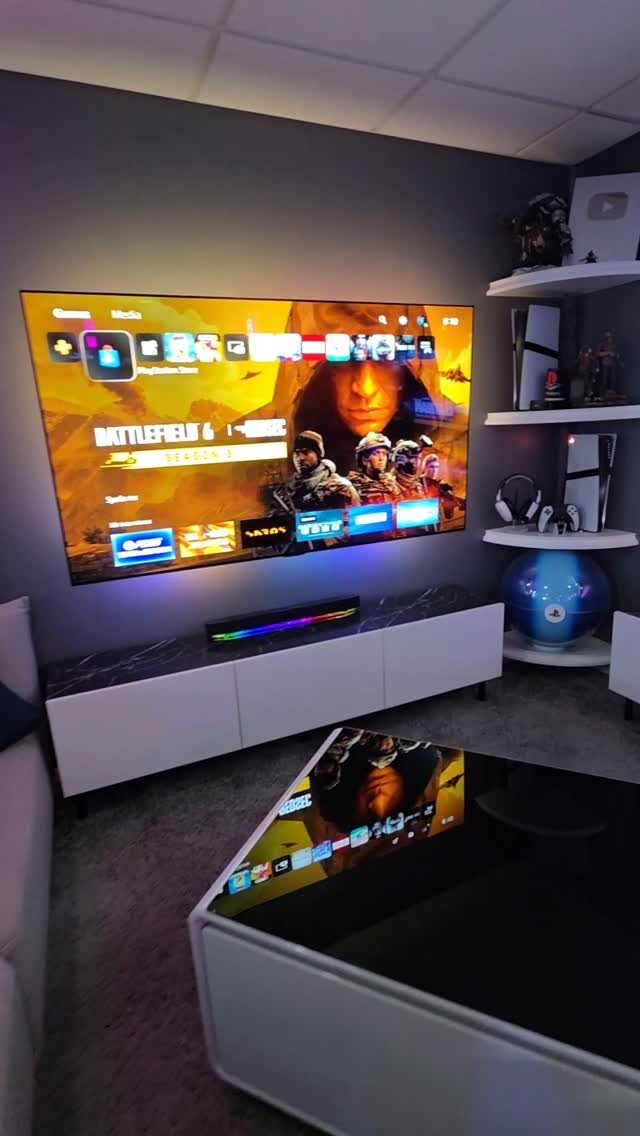 Large television displaying a game menu above a white console in a grey room.