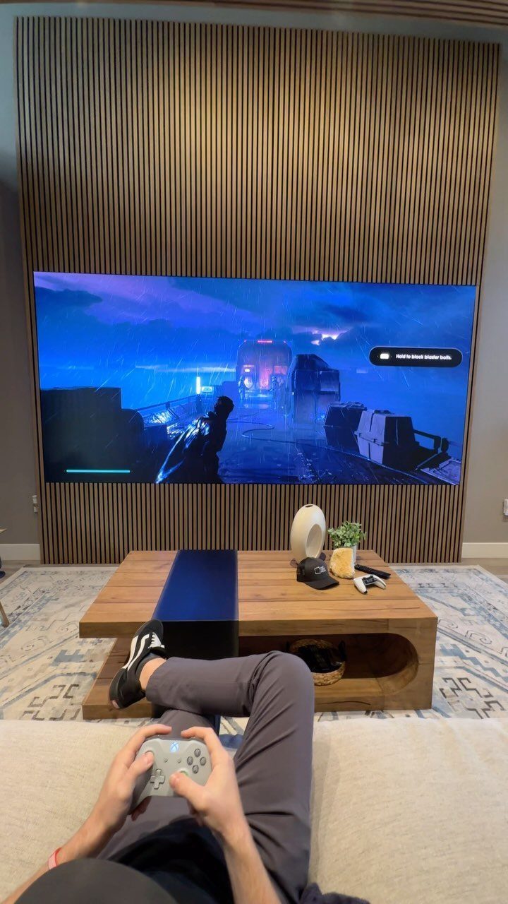 Person playing a video game on a large screen against a wooden wall.