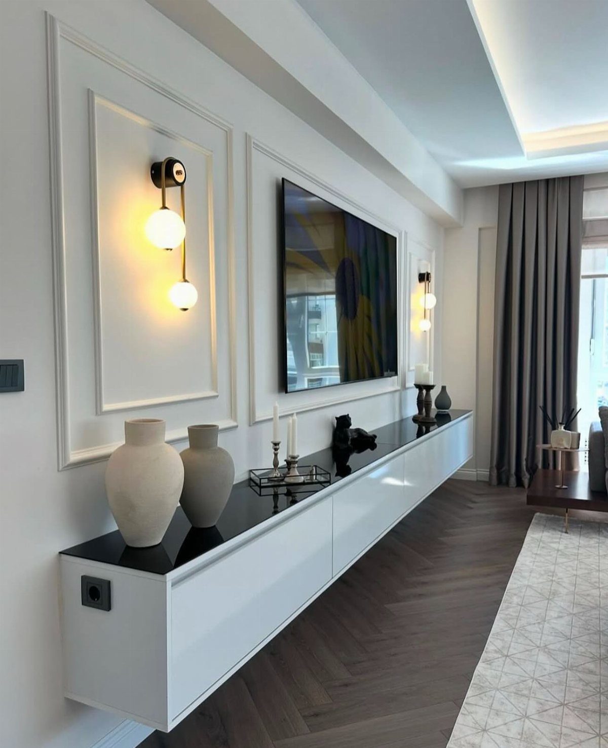 Two glowing globe wall sconces flanking a flat-screen TV above a white console.