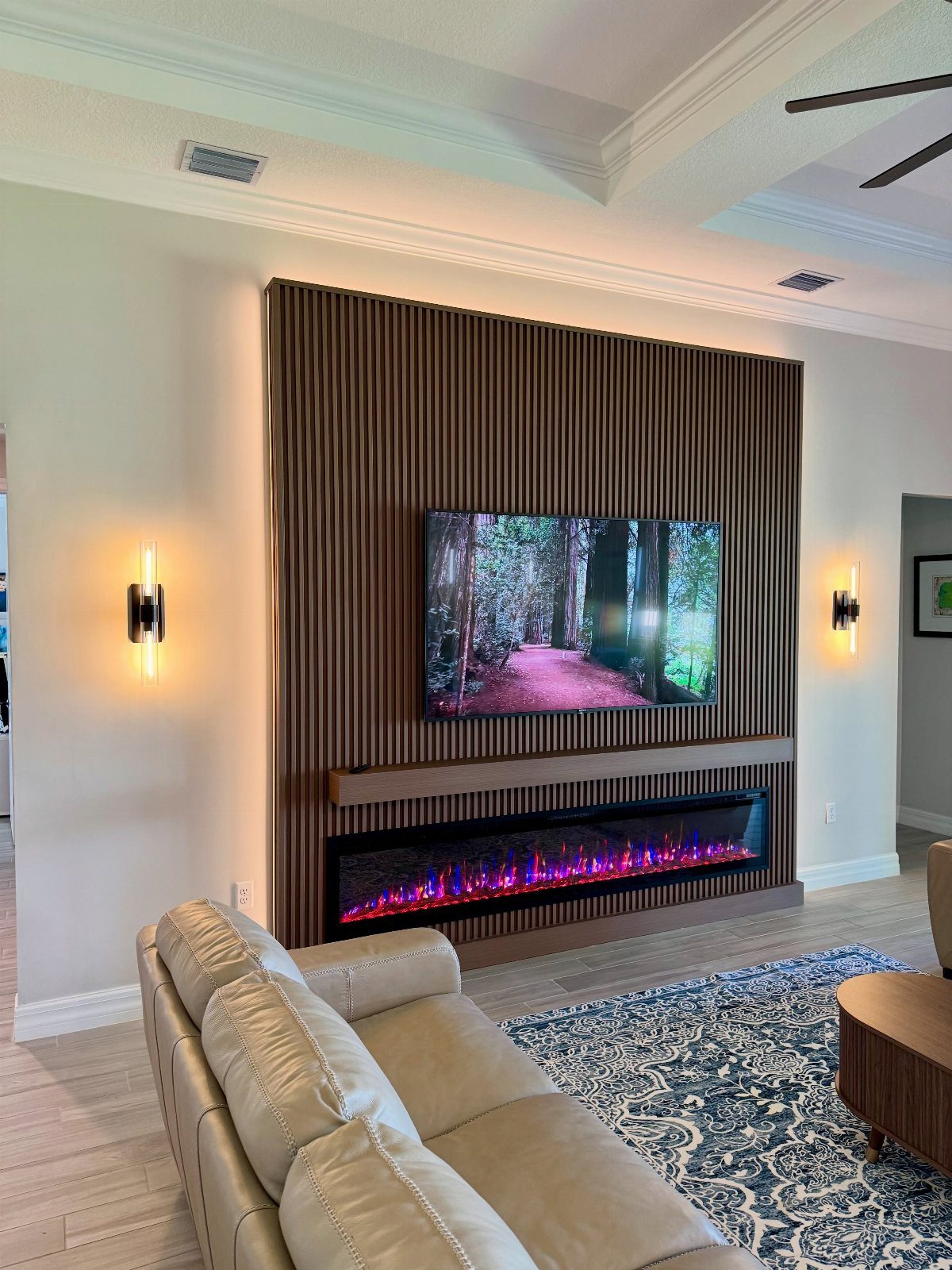 Two vertical wall sconces flanking a TV on a slatted wood wall with fireplace.