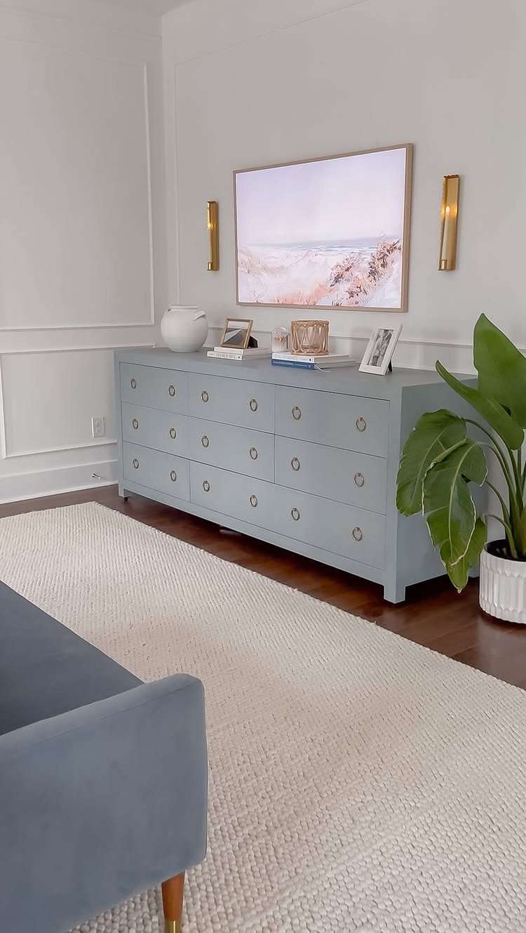 Gold wall sconces flanking a painting above a light blue dresser in a room.
