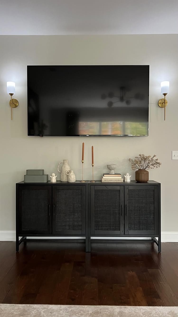 Wall sconces with white shades flanking a mounted TV above a black sideboard.