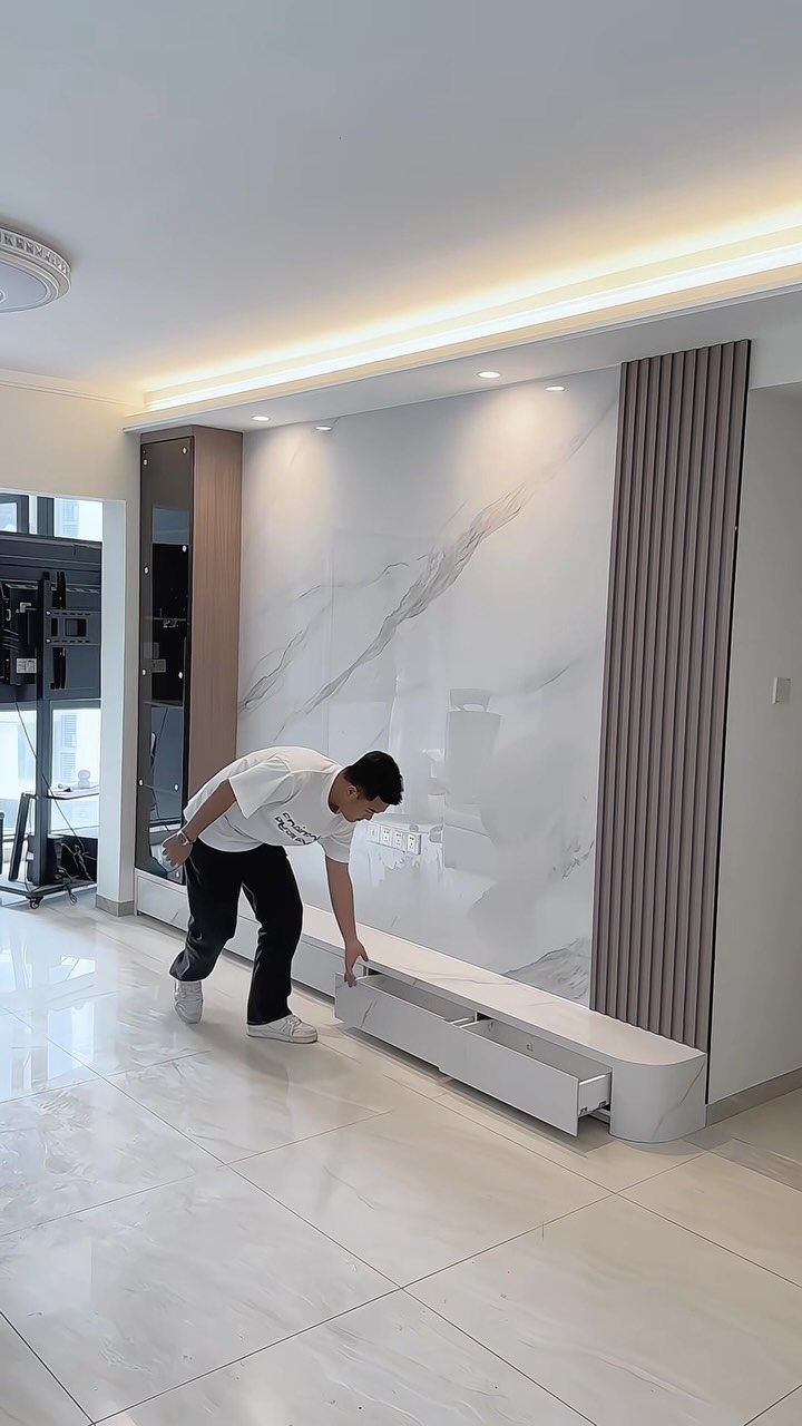 White floating TV console with open drawer against a marble wall and wooden slats.