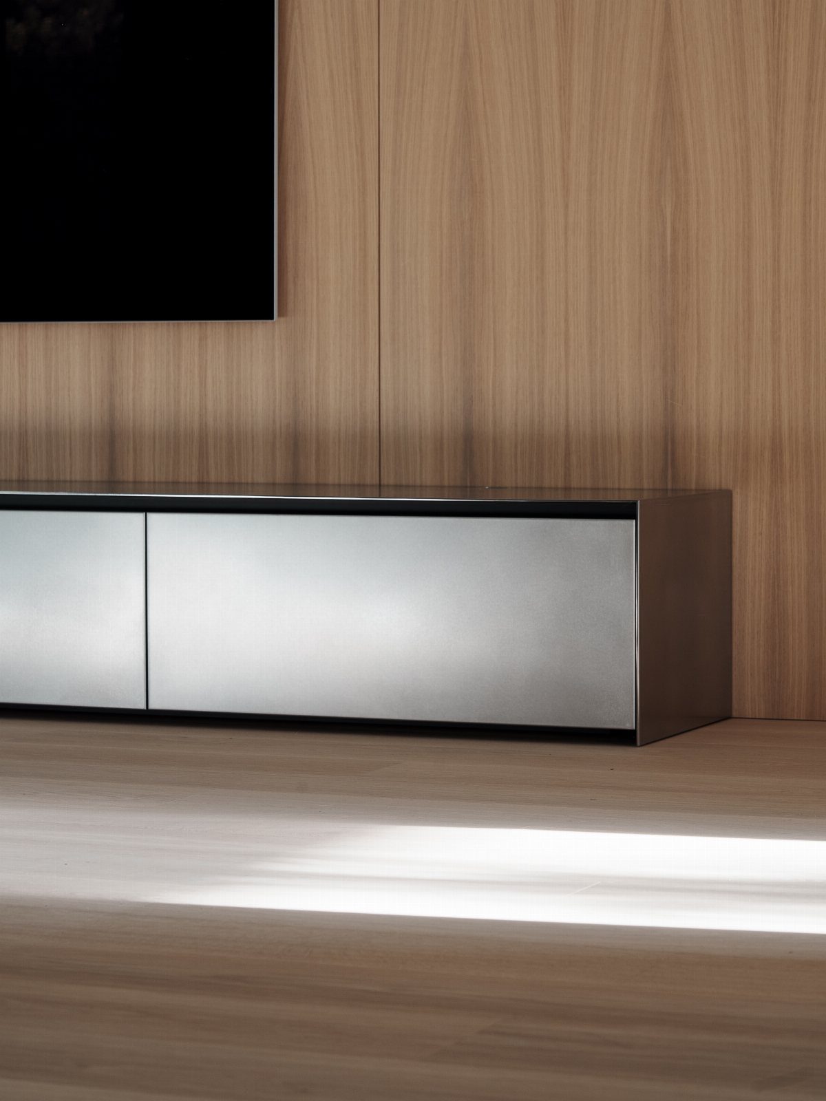 Silver metal TV console against a light wood paneled wall and floor.