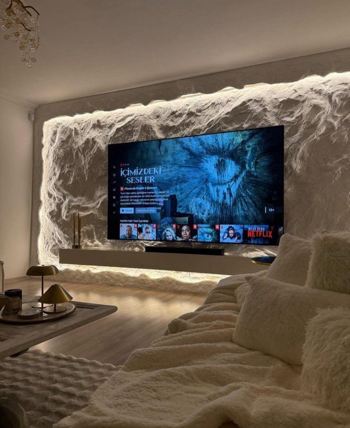 Textured stone-finish TV background wall with LED lighting and a floating white shelf.
