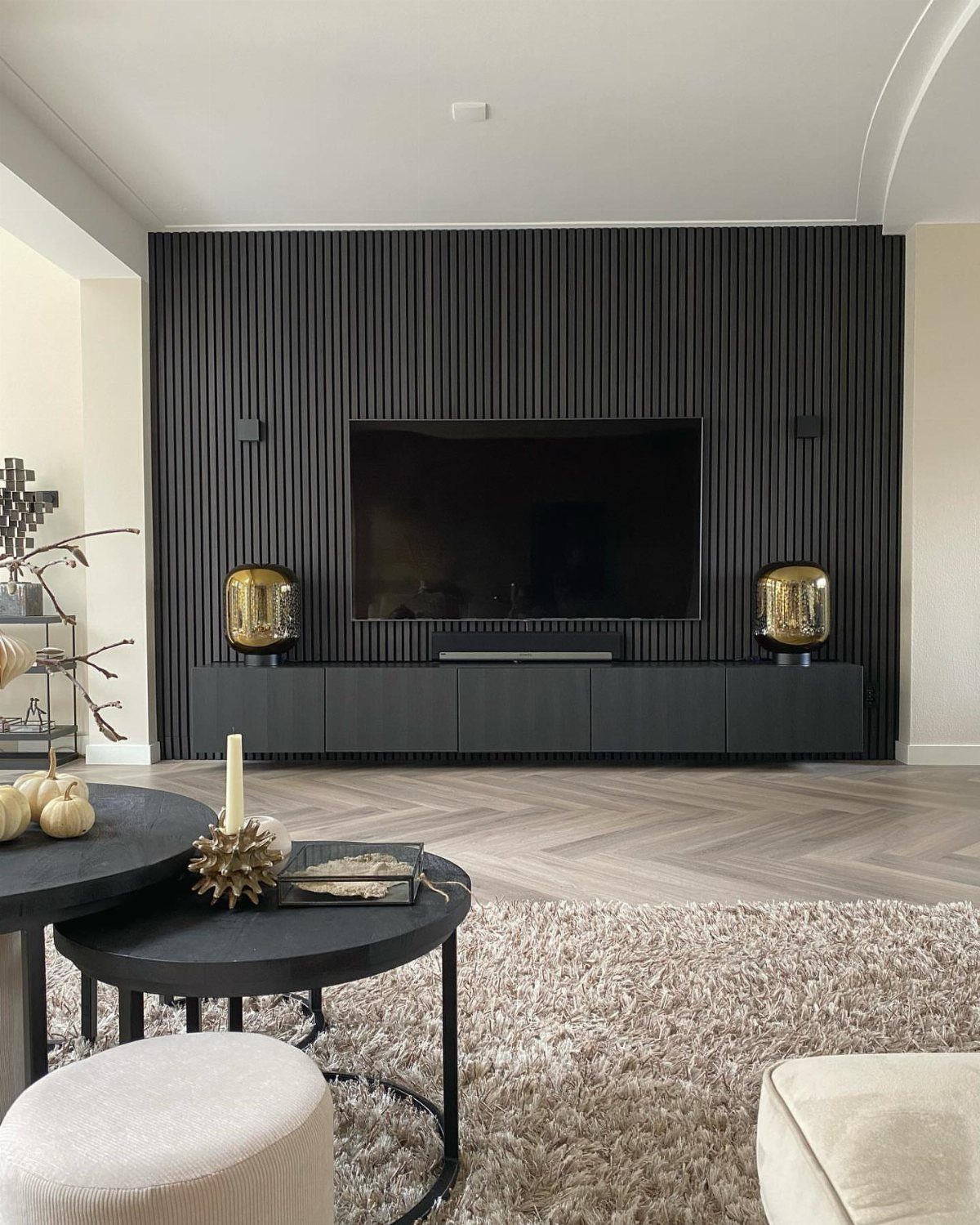 Black vertical wood slat wall paneling behind a large television and black console.