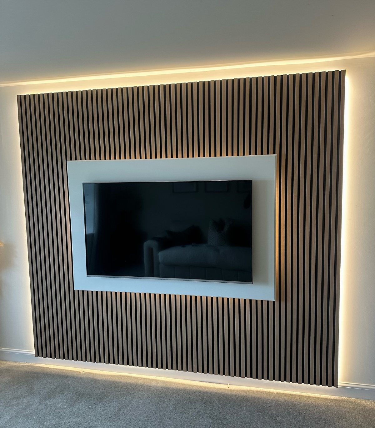 Television mounted on a white panel against vertical brown wood slat wall paneling
